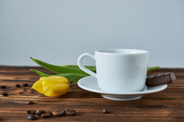 cup of coffee and yellow tulip on wooden background, close up