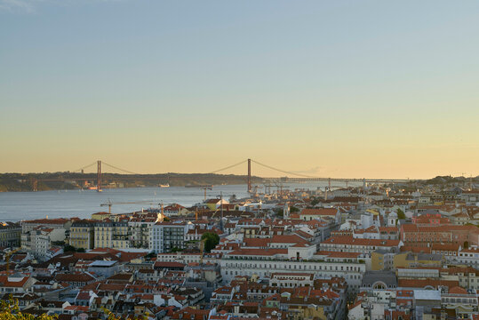 Panoramic view of a cityscape with a large 25 de Abril Bridge under a clear sky at sunset. Lisbon, Portugal