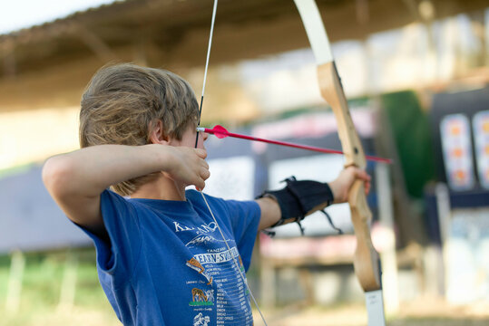 Young boy aiming a bow and arrow at a target outdoor during an archery lesson Israel