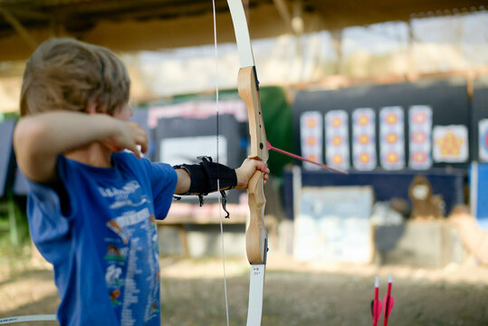 Child practicing archery, aiming a bow with arrows at a target in an outdoor range. Israel
