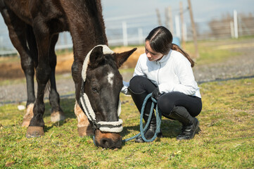 Young jockey crouching and holding reins while horse is grazing in paddock