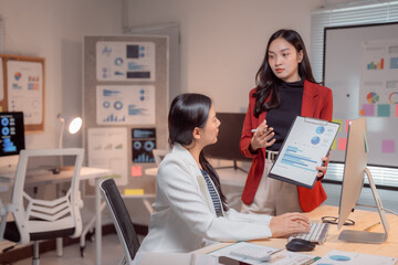 Two young businesswomen are analyzing financial charts and graphs while discussing company strategy...