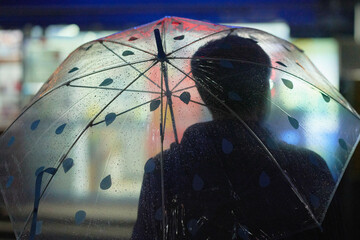 Silhouette under transparent umbrella with raindrop pattern against blurred urban lights. Busan, Korea