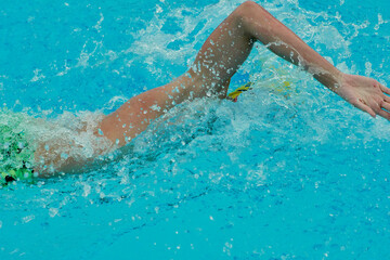 Triathlon swimmer in green shorts performing front crawl in a blue pool with splashing water.