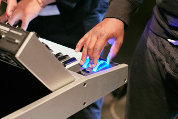 Close-up of hands playing on an electronic keyboard with a blue illuminated button.
