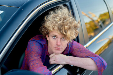 Person with curly hair leans out of a car window, wearing a purple patterned shirt. Miami, FL, USA