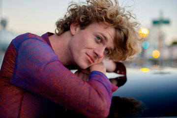 A person with curly hair wearing a purple top leans on a reflective surface outdoors. Miami, FL, USA