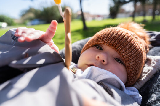 Baby wearing knitted hat relaxing in stroller at park