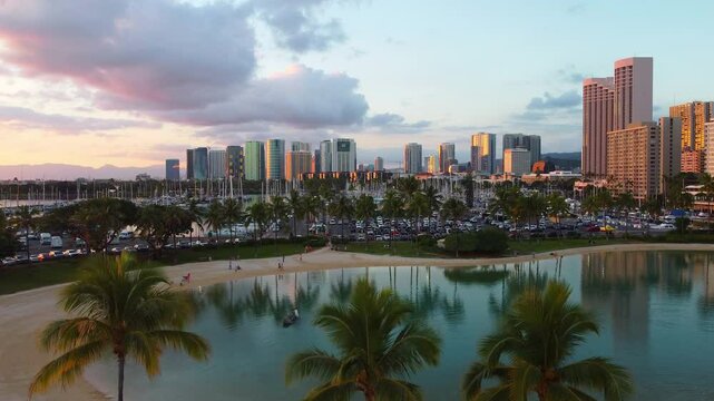 Ala Wai Boat Harbor at sunset, Honolulu skyline reflecting golden light, palm trees lining Ala Moana beach with calm waters and yachts