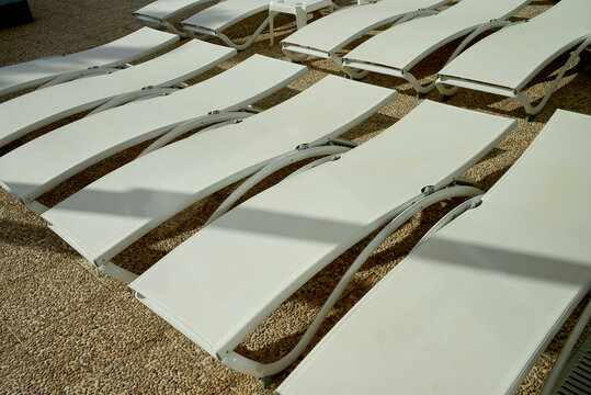 Sunlit row of white poolside loungers on a pebble surface in a sunny outdoor setting. Lanzarote, Spain
