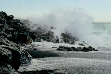 Powerful ocean waves crash against rugged black rocks on a cloudy coastal day. Lanzarote, Spain