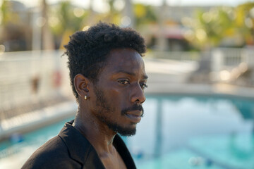 Contemplative man by a swimming pool with blurred palm trees in the background. Miami, Florida