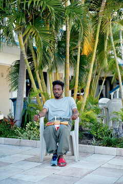 Man sitting on a chair outside, surrounded by palm trees and preparing a peanut butter sandwich. Miami, Florida