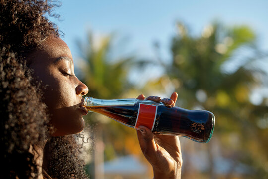 Woman enjoying a refreshing drink from a glass bottle outdoors in sunny weather. Miami, Florida, USA