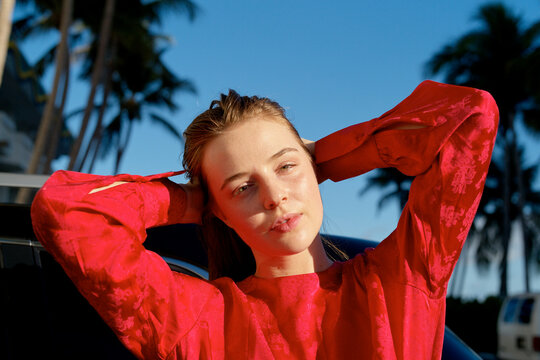 Woman in a red shirt poses outdoors with palms and blue sky in the background. Miami, FL, USA