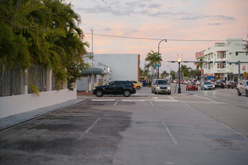 Urban street at sunset with parked cars, palm trees, and colorful buildings lining the road. Miami, FL, USA
