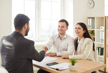 Young happy smiling business people sitting at the desk in modern office and making a deal shaking hands with colleagues on meeting. Coworkers reaching agreement. Partnership concept.