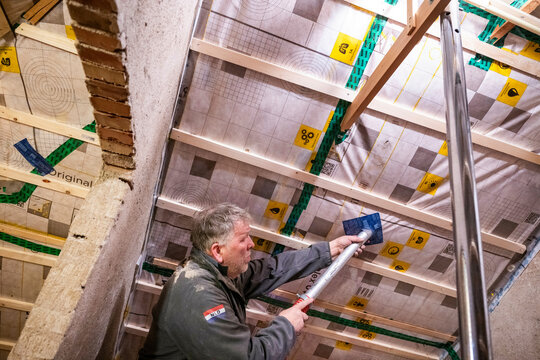 Man installing insulation in a ceiling framework in a construction setting. Netherlands