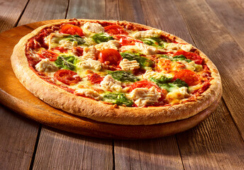 Holzofenpizza mit Huhn Tomaten und Pesto auf rundem Holzbrett und rustikaler Holzplatte, Italien,...