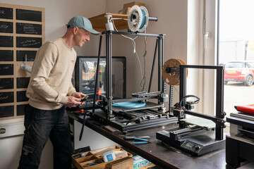 Man operating a 3D printer in a bright workspace, with tools and materials around. Nijmegen, Netherlands