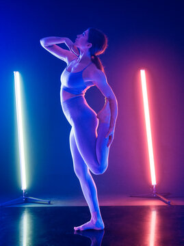 Female dancer performs a standing yoga pose under neon blue and pink lights onstage.