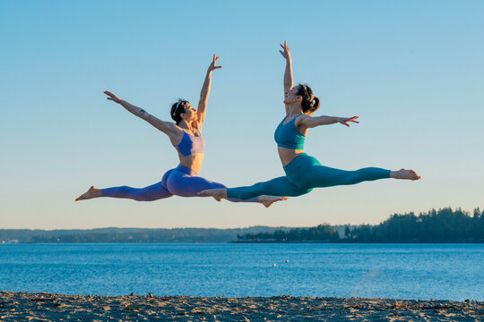 Two women performing elegant ballet leaps on a beach with a scenic ocean backdrop, Lytle Beach, Bainbridge Island, WA, USA