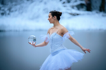 Ballerina in a white tutu holds a crystal ball in a snowy, serene winter landscape. WA, USA