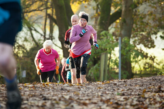 Adults running uphill in a park, wearing athletic clothing, surrounded by autumn foliage and fallen leaves. Sale Water Park, Manchester, UK