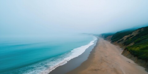 A foggy beach with a blue ocean in the background. The sky is overcast and the beach is empty