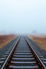 Fototapeta premium A train track is shown in the fog with a few trees in the background. Concept of mystery and solitude, as the fog obscures the surroundings and the train tracks seem to stretch on endlessly