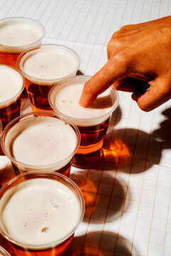man with his forefinger in a plastic cup with beer
