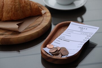 Tip and receipt near croissant on wooden table, closeup