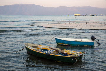 Obraz premium Quiet evening with fishing boats anchored near the shore in Albania against a backdrop of gentle waves and distant hills