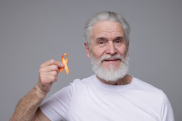 Multiple Sclerosis awareness. Senior man with orange ribbon on grey background