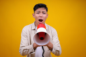 Angry Young Man Shouting On Megaphone Over Yellow Background