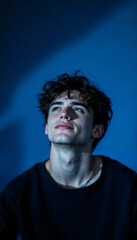 Young man in dark blue lighting gazing upwards dreamily.