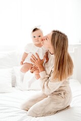 a mother with a newborn baby in her arms at home on a white background of a bed or window, a space for text, a young mother gently kisses and hugs her baby, maternal love
