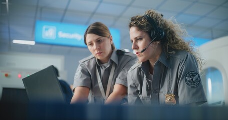Naklejka premium Airport Security Checkpoint: Female TSA Officer Wearing Headset Uses Laptop, Talks to Colleague. Transportation Security Administration for Travel Safety. In the Background, Airport Staff Working.