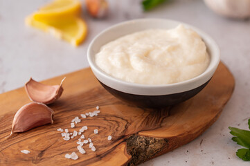 Lebanese Garlic sauce Toum or Salsat toum contains garlic, salt, olive oil and lemon juice on wooden board. Traditional Middle East food. Food photography.