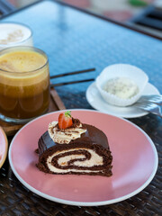 Slice of chocolate cake is on a pink plate next to a cup of coffee