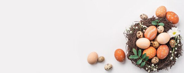 Easter nest with hand-painted eggs and quail eggs on a light background. A rustic spring composition with natural elements, fresh greenery and floral details.