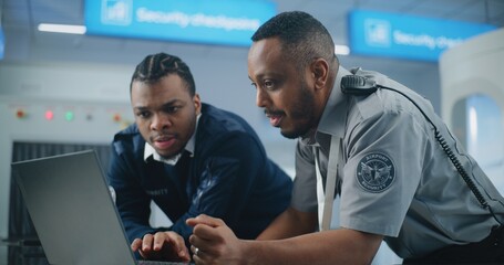 Airport Security Checkpoint: African American TSA Workers Using Laptop, Discussing Security Issues....