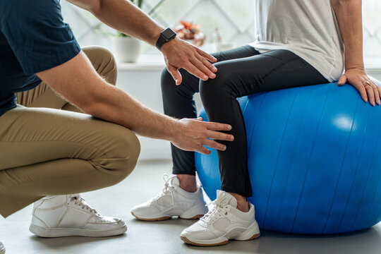 Physiotherapist helping senior woman with leg rehabilitation exercise on balance ball