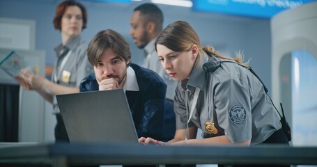 Airport Security Checkpoint: Two Diverse TSA Workers Using Laptop, Discussing Security Issues....
