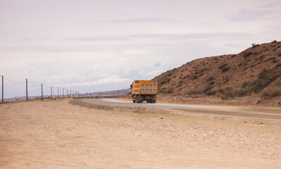 orange truck on the dusty sandy road, mountains barely visible in the distance, construction site, building