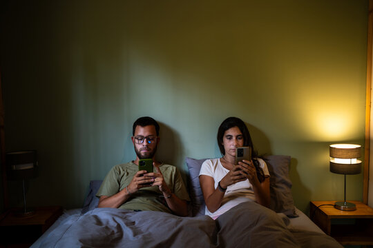 young Couple Using their phones in Comfortable Bedroom