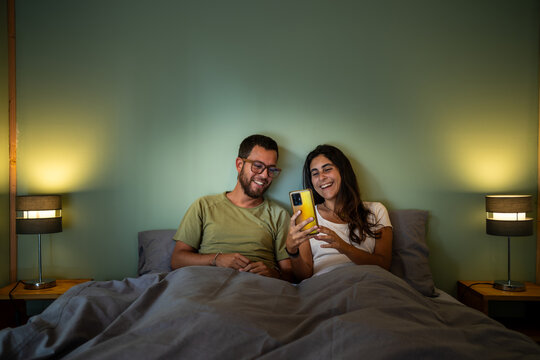 Smiling Couple Enjoying scrolling on phone in Cozy Bed