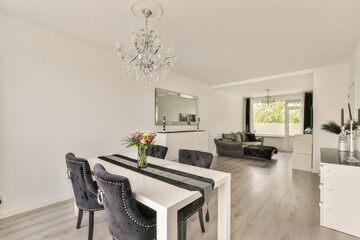 A bright and stylish interior featuring a modern dining table, plush black chairs, and a cozy living area with large windows, perfect for contemporary living.