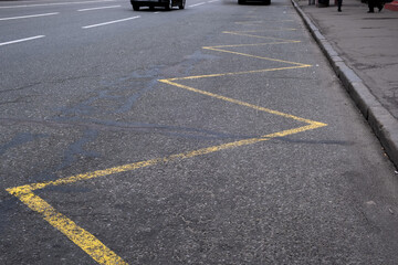 This closeup shows a zigzag pattern of bright yellow lines on a busy city street, highlighting important traffic markings that guide vehicles and supporting urban movement in the bustling metropolis