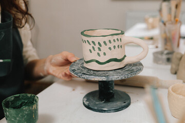 Painter is drawing and making a colorful decoration of a clay ware. Female artist is painting earthenware with paintbrush and water colors in the workshop.